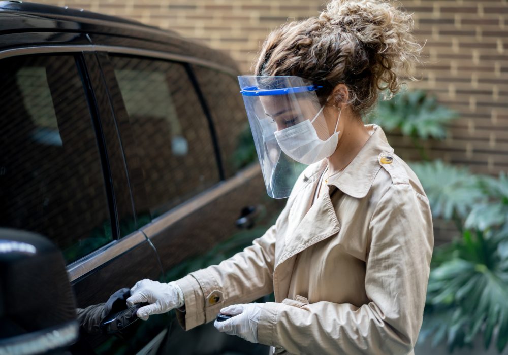 Latin American woman opening her car wearing a facemask and a face shield during the COVID-19 pandemic â transportation concepts